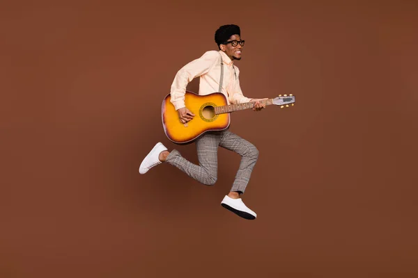 Eğlendirici adamın fotoğrafı. Zıplama, gitar çalma melodisi. Pantolon askısı ayakkabıları, izole kahverengi arka plan. — Stok fotoğraf