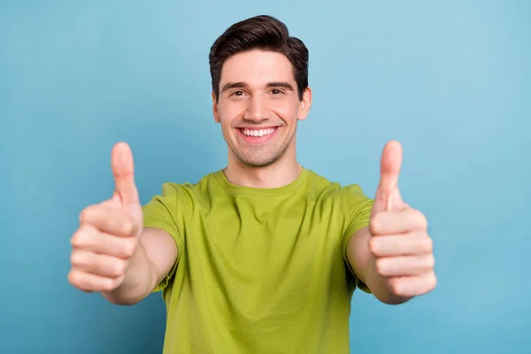 Fénykép imádnivaló édes fiatalember visel zöld póló mosolygós mutatja hüvelykujj fel elszigetelt kék színű háttér — Stock Fotó