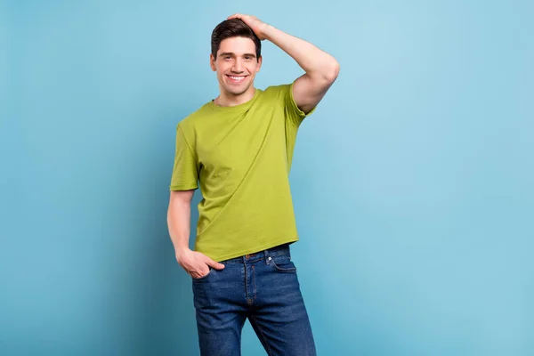 Foto von netten jungen brünetten Kerl Handhaar tragen grüne T-Shirt Jeans isoliert auf blauem Hintergrund — Stockfoto