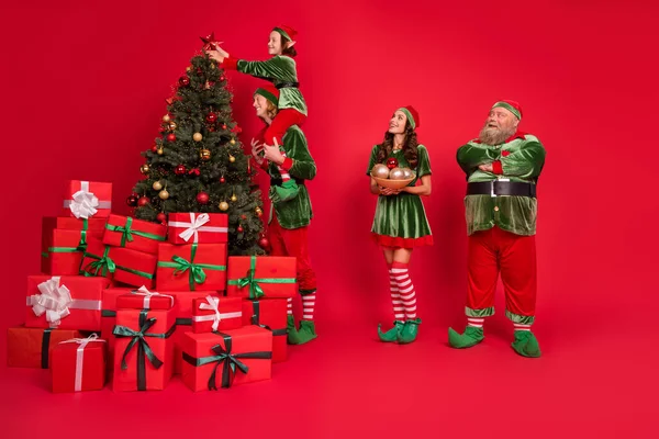 Pełna długość ciała rozmiar widok modnych przyjaciół przyjaźń wesołe elfy dekorowanie festal drzewa dzień izolowany na jasnoczerwony kolor tła — Zdjęcie stockowe