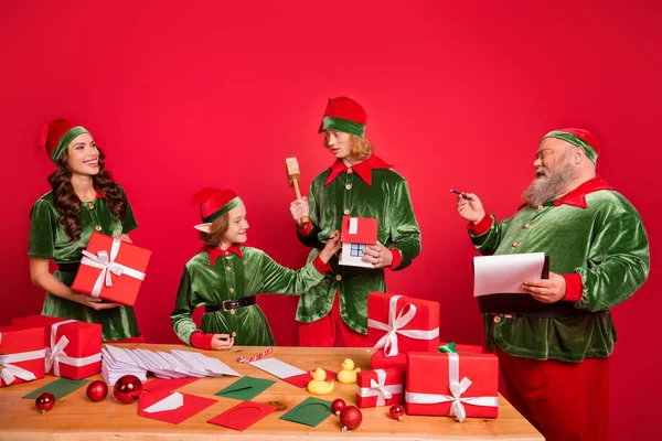 Portrait of four trendy cheerful elfs preparing gift list order dream delivery isolated over bright red color background — Stock Photo, Image