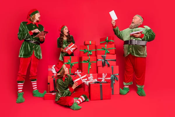 Noel Baba asistanlarının tam boy fotoğrafı. İnsanlar kızgın. Hediye kutuları kırmızı arka planda izole edilmiş yeni yıl kostümleri giyerler. — Stok fotoğraf