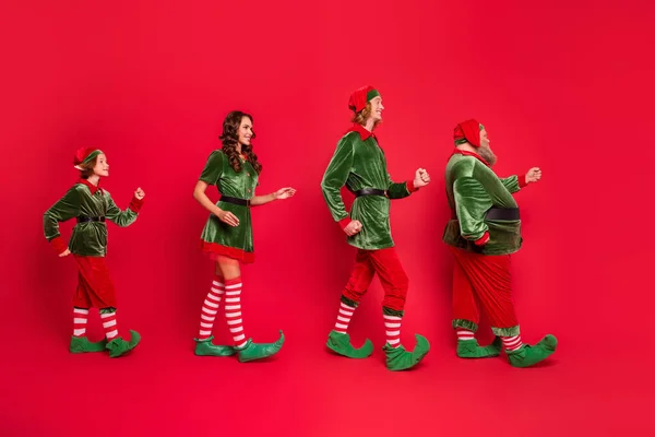 Foto de longitud completa de positiva alegre santa helper elfo Navidad desgaste sombrero ir vacío espacio milagro aislado sobre fondo de color rojo —  Fotos de Stock