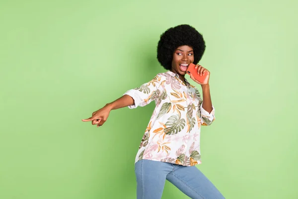 Foto av ung afrikansk flicka glad positiva leende sjunga mikrofon peka finger tomt utrymme isolerad över grön färg bakgrund — Stockfoto