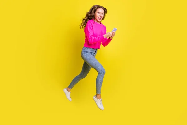 Фотографія повної довжини блискучої леді, одягнена в рожевий пуловер, що йде, стрибає з високим типом сучасного пристрою ізольований жовтий кольоровий фон — стокове фото
