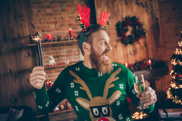 Photo of inspired bearded guy hold glass champagne bengal fire wear deer headband pullover decorated home indoors