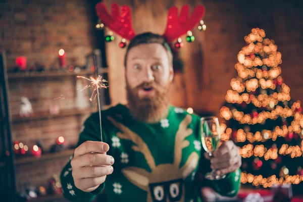 Photo of crazy funny funky guy hold glass champagne bengal fire wear reindeer headband jumper decorated home indoors