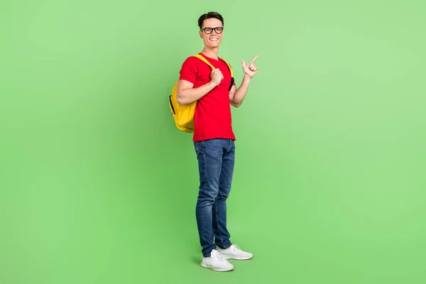 Fénykép vicces csinos fiatal srác öltözött piros póló szemüveg mutató ujj üres tér mosolygós elszigetelt zöld színű háttér — Stock Fotó