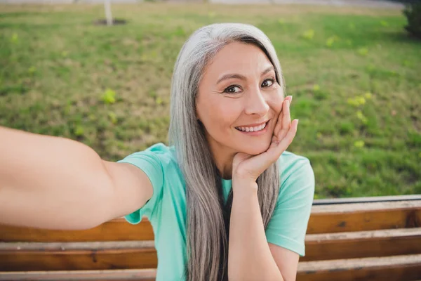 Foto do aposentado alegre sonho velha senhora sentar banco mão queixo atirar selfie desgaste teal t-shirt urbana cidade ao ar livre — Fotografia de Stock