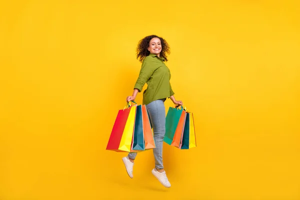 Photo of positive funny funky attractive beautiful stylish lady wear green shirt jumping holding colorful bargains isolated yellow color background — Stock Photo, Image