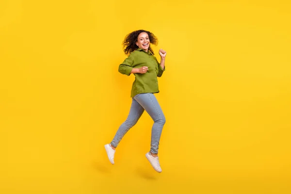 Foto de positivo bonito funky engraçado enérgico mulher vestida camisa verde saltando alta corrida sorrindo isolado cor amarela fundo — Fotografia de Stock