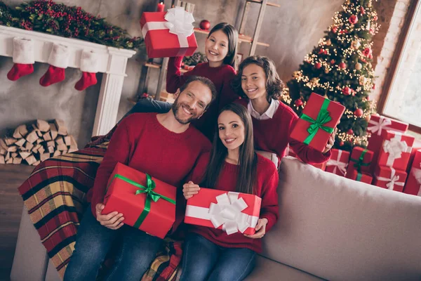Zdjęcie radosnego męża żona dzieci trzymać prezenty siedzieć na kanapie nosić czerwony sweter dżinsy wewnątrz w Wigilię — Zdjęcie stockowe