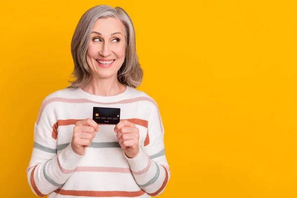 Photo of sweet charming lady pensioner wear striped pullover holding credit card looking empty space isolated yellow color background — Stock Photo, Image