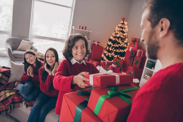 Foto di eccitato grazioso papà mamma due bambini vestiti maglioni rossi in attesa di nuovo anno presenta sorridente casa interna stanza — Foto Stock