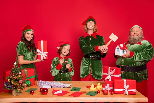 Ritratto di quattro attraenti amici allegri elfi Santa helper preparare regali vigilia giorno isolato su sfondo di colore rosso brillante — Foto Stock