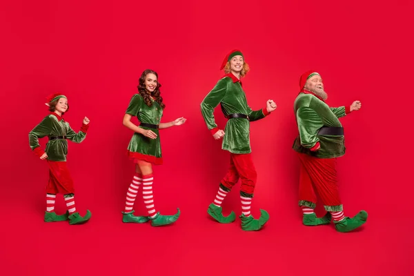 Helkroppsfoto av glad Santa Helper promenad gå tomt utrymme xmas humör bära hatt isolerad på röd färg bakgrund — Stockfoto