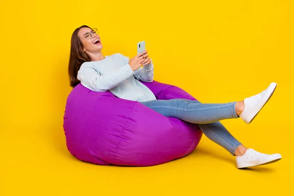 Foto de longitud completa de la feliz mujer alegre disfrutar de sentarse silla sostener teléfono risa broma comentario aislado sobre fondo de color amarillo — Foto de Stock