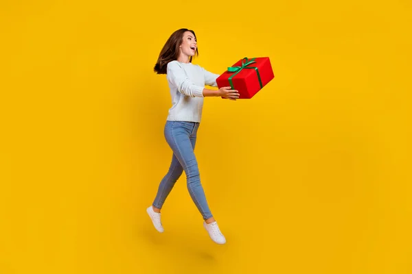 Photo pleine grandeur de heureuse jeune femme étonnée sauter tenir la main cadeau de vacances isolé sur fond de couleur jaune — Photo