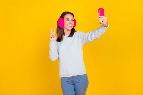 Foto de mujer joven feliz positiva usar calentador de oído hacer teléfono selfie aislado en el fondo de color amarillo — Foto de Stock