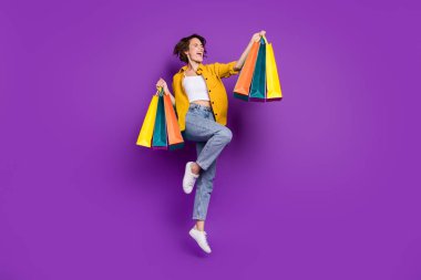 Full length body size view of attractive cheerful girl jumping carrying bags isolated over bright violet purple color background clipart