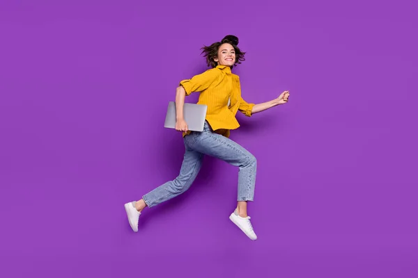 Foto de brilhante muito jovem mulher vestida camisa amarela sorrindo pulando correndo segurando dispositivo moderno isolado cor roxa fundo — Fotografia de Stock