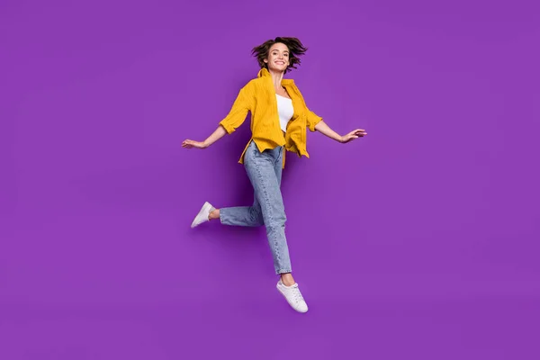 Foto de engraçado doce jovem senhora usar camisa amarela saltando alto sorrindo isolado cor violeta fundo — Fotografia de Stock