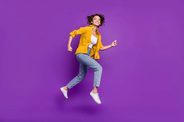 Foto de adorável brilhante jovem mulher vestida camisa amarela sorrindo saltando alto correndo rápido isolado cor roxa fundo — Fotografia de Stock