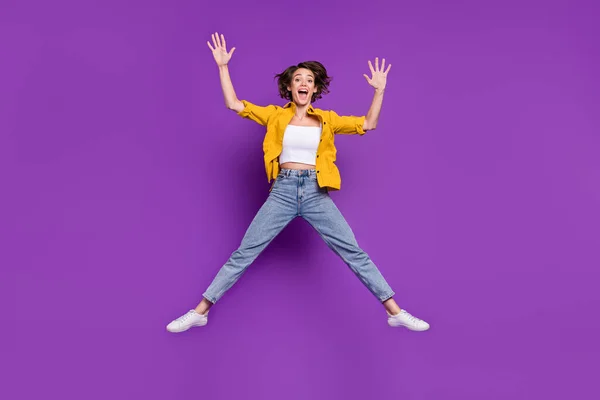 Фото чарівної смішної молодої леді в жовтій сорочці, що стрибає з високою посмішкою ізольований фіолетовий кольоровий фон — стокове фото