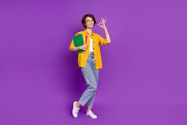 Full length body size view of attractive cheery girl holding materials showing ok-sign isolated over bright violet purple color background — Stock Photo, Image