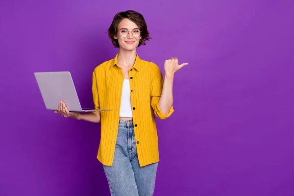 Ritratto di attraente ragazza allegra di tendenza che tiene il computer portatile mostrando lo spazio di copia isolato su luminoso viola sfondo di colore viola — Foto Stock
