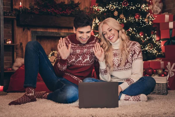 Foto penuh pasangan optimis menyapa pada laptop duduk di karpet memakai celana jeans jumper di dalam ruangan pada malam x-mas — Stok Foto