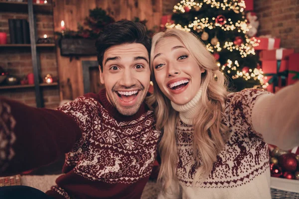 Foto de pareja divertida hacen selfie desgaste feo año nuevo suéteres en el interior cerca del árbol en x-mas víspera — Foto de Stock