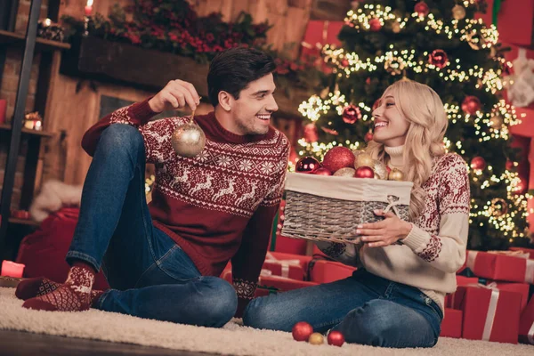 Zdjęcie atrakcyjne śmieszne młoda żona mąż nosić druk swetry uśmiechnięty dekorowanie noel drzewa w domu dom pokój — Zdjęcie stockowe