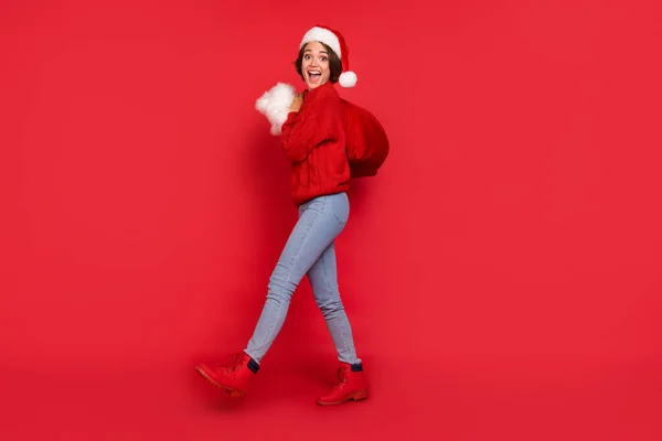 Full length body size φωτογραφία όμορφη γυναίκα σε headwear τσάντα μεταφοράς με δώρα απομονώνονται ζωντανό κόκκινο χρώμα φόντο — Φωτογραφία Αρχείου