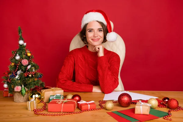 Фотопортрет молодої жінки, посміхаючись, сидить за столом в головній убірці ізольований яскраво-червоний кольоровий фон — стокове фото