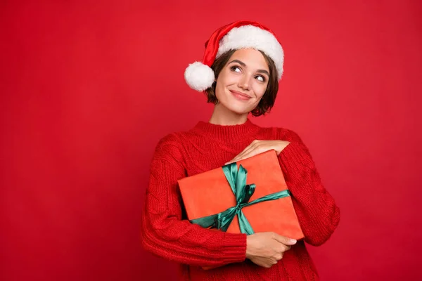 Φωτογραφία πορτρέτο νεαρή γυναίκα κρατώντας δώρο Χριστούγεννα στο καπέλο αναζητούν copyspace απομονωμένο φωτεινό κόκκινο χρώμα φόντο — Φωτογραφία Αρχείου