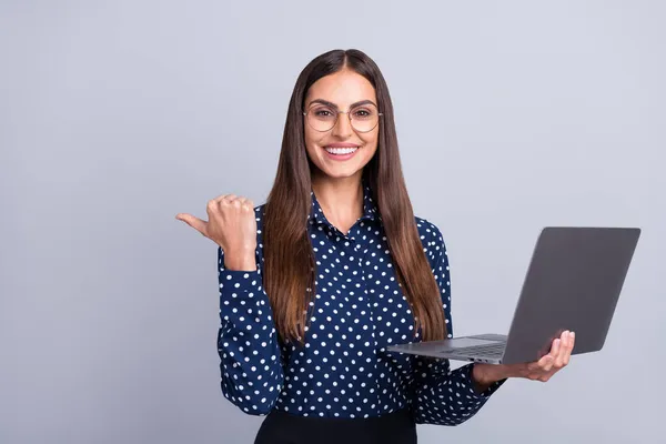 Foto der netten jungen brünetten Dame halten Laptop Punkt leeren Raum tragen blaues Hemd Brille isoliert auf grauem Hintergrund — Stockfoto