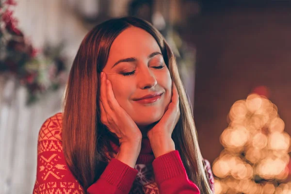 Φωτογραφία από στοχαστική ονειρεμένη νεαρή γυναίκα ντυμένη κόκκινο πουλόβερ γιορτάζει το νέο έτος κλειστά μάτια χαμογελώντας σε εσωτερικούς χώρους σπίτι δωμάτιο — Φωτογραφία Αρχείου
