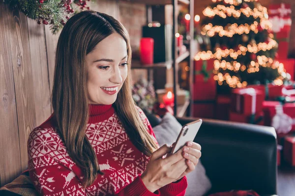 Фото збудженої красивої зрілої леді в червоній пуловері, посміхаючись, пишучи сучасні гаджети різдвяні привітання в приміщенні домашньої кімнати будинку — стокове фото