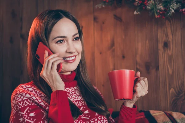 Foto av rolig ganska mogen dam bära röd pullover ler talar modern gadget dricka jul dryck inomhus hus hem rum — Stockfoto