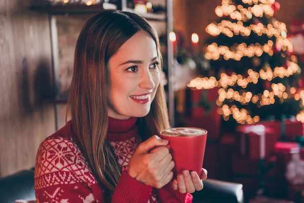 Φωτογραφία από γλυκό στοχαστικό νεαρή γυναίκα ντυμένη κόκκινο πουλόβερ πίνοντας το νέο έτος ποτό χαμογελώντας εσωτερικό δωμάτιο σπίτι — Φωτογραφία Αρχείου