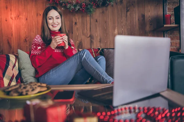 Foto av glänsande drömmande mogen dam bära röd pullover dricka äggtoddy titta på modern anordning jul program inomhus hus hem rum — Stockfoto