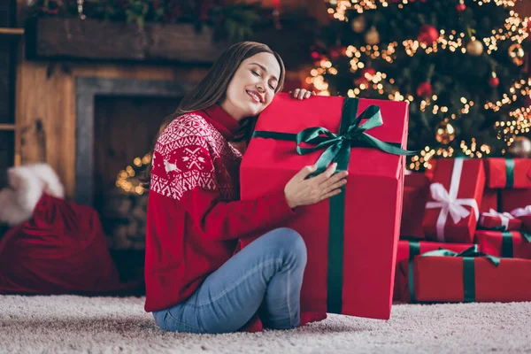 Φωτογραφία από ονειρεμένη γλυκιά νεαρή γυναίκα ντυμένη κόκκινο πουλόβερ αγκαλιάζει το νέο έτος μεγάλο κουτί δώρου χαμογελώντας σε εσωτερικούς χώρους σπίτι δωμάτιο — Φωτογραφία Αρχείου