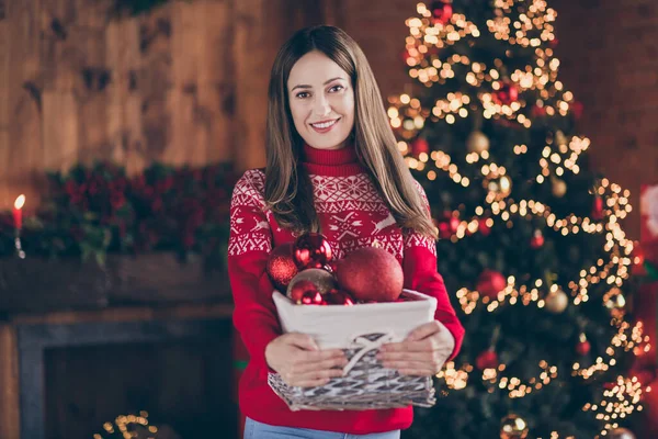 Фото чарівної блискучої молодої жінки, одягненої в червоний светр, прикрашає новорічну ялинку, посміхаючись в приміщенні домашнього будинку — стокове фото