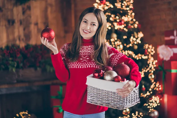 Foto av glänsande positiv ung kvinna klädd röd tröja håller nytt år dekorationer ler inomhus rum hem hus — Stockfoto