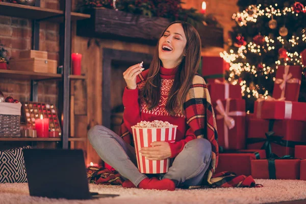 Photo of pretty funny young woman dressed red sweater eating popcorn watching modern gadget new year film smiling indoors room home house — Stock Photo, Image