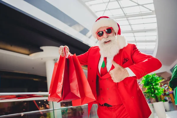 Фото уверенного Санта-Клауса носить темные очки проведение сделок показывая большой палец вверх внутри торгового центра — стоковое фото