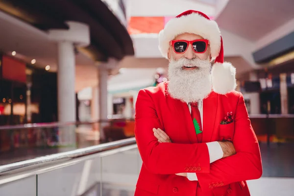 Фото уверенного смешного Санта сложил руки подготовить рождественские подарки носить солнцезащитные шляпы красный смокинг в торговом центре супермаркета — стоковое фото