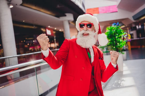 Foto de sorte funky santa claus usar óculos escuros levantando punhos sorrindo dentro de casa loja boutique — Fotografia de Stock