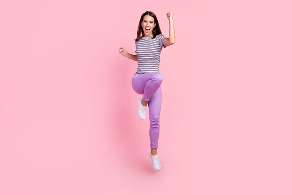 Foto de afortunada joven bonita usar traje a rayas sonriente saltando puños de gran altura aislado de color rosa de fondo —  Fotos de Stock